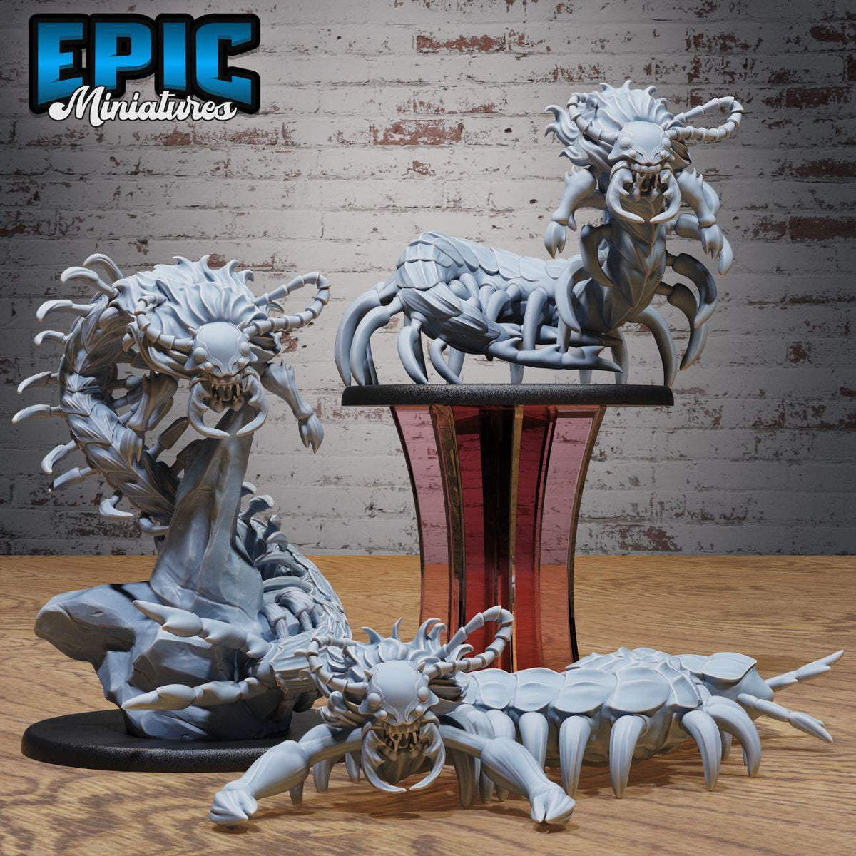 three detailed figurines of fantastical creatures, including a large, menacing-looking creature with sharp teeth and claws, as well as two smaller, more intricate creatures. The figurines are displayed on a wooden surface, with a brick wall in the background.