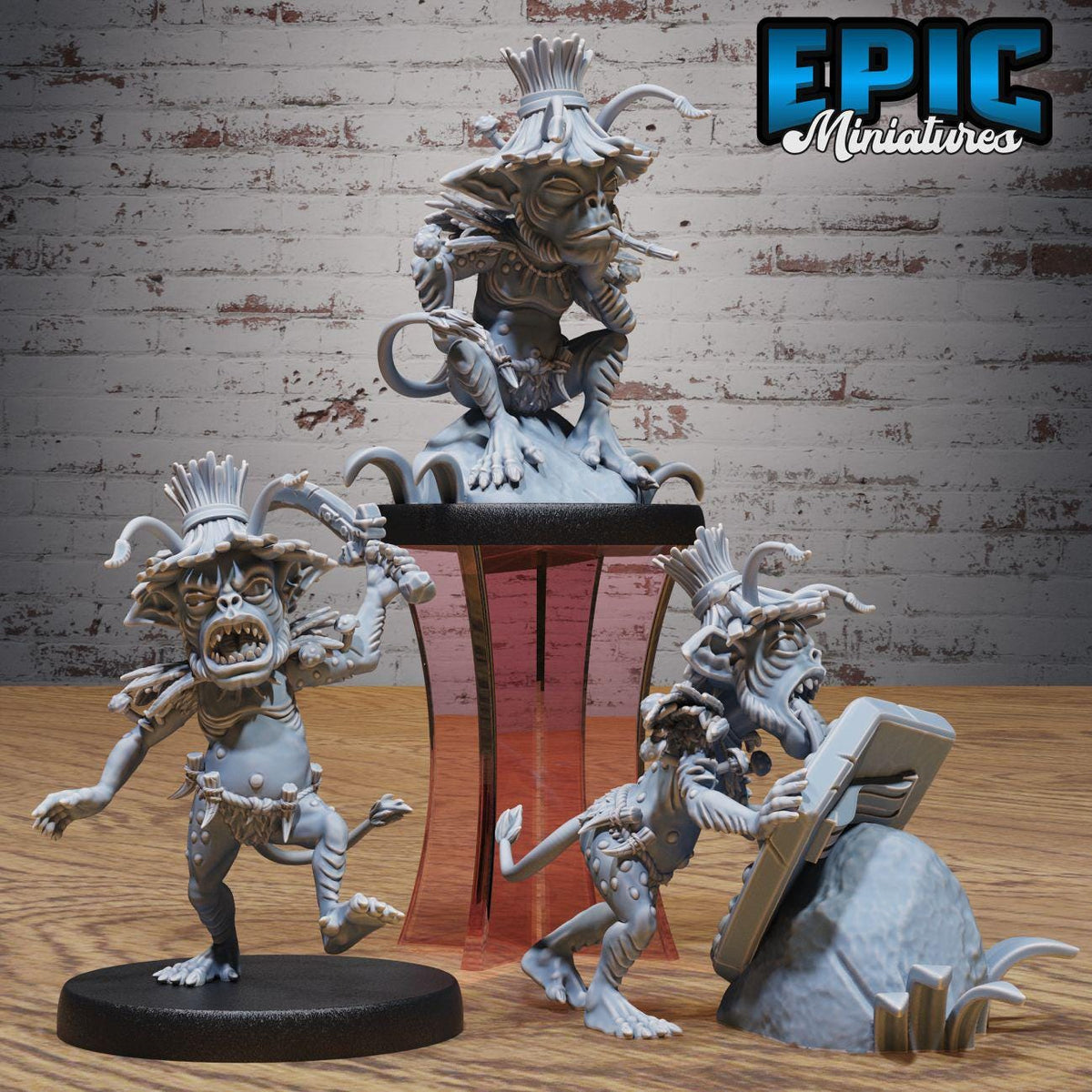 three figurines of fantastical creatures, including a dragon-like creature, a humanoid creature with horns, and a creature with a long tail. The figurines are displayed on a wooden surface against a brick wall background.