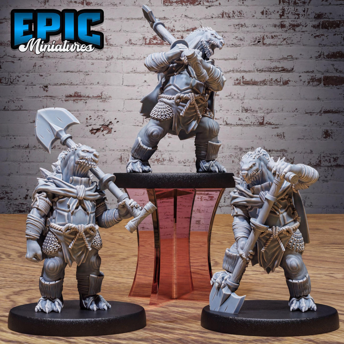 three miniature figures of fantasy creatures, each holding various weapons, standing on a platform against a brick wall background.