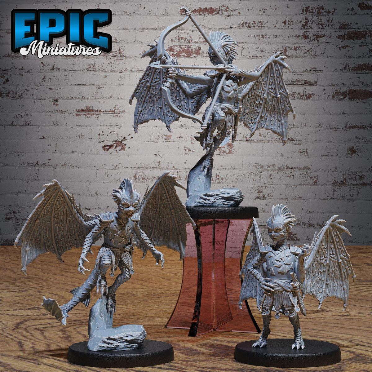 three detailed figurines of winged creatures, possibly mythical or fantasy-inspired, displayed on a wooden surface against a brick wall background.