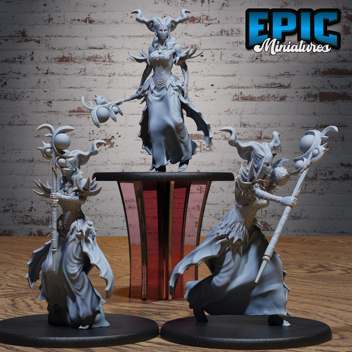 three figurines of fantastical creatures, including a large, winged figure with horns and a flowing dress, and two smaller figures with similar elaborate costumes and weapons.