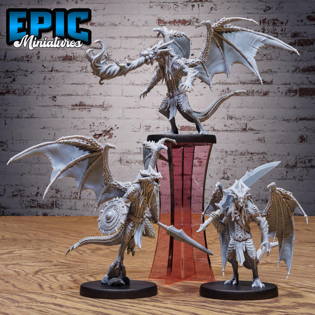 three figurines of fantastical creatures, including winged creatures and armored figures, displayed on a wooden surface against a brick wall background.