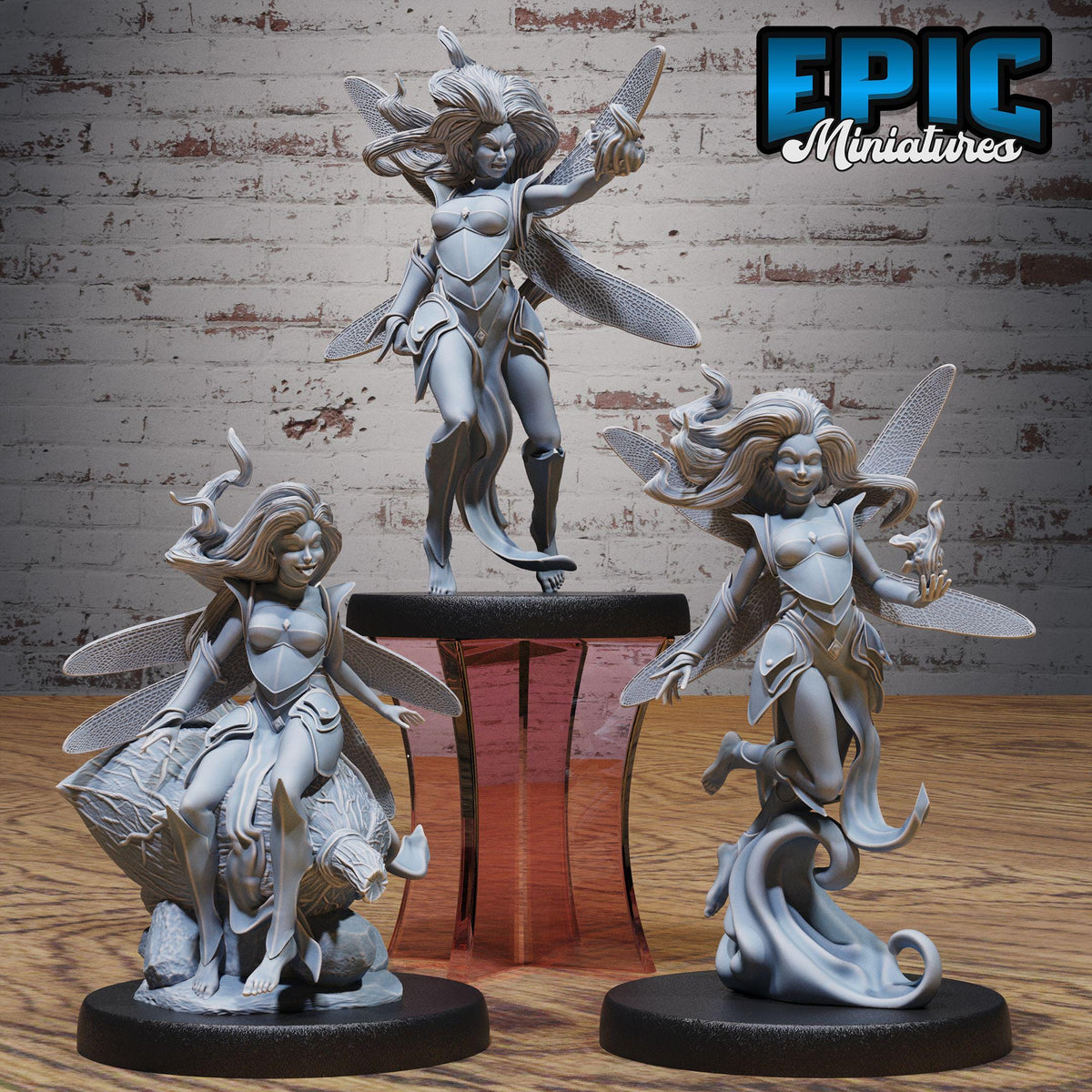 three figurines of winged female characters, each with distinct poses and expressions, displayed on a wooden surface against a brick wall background.