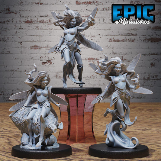 three figurines of winged female characters, each with distinct poses and expressions, displayed on a wooden surface against a brick wall background.