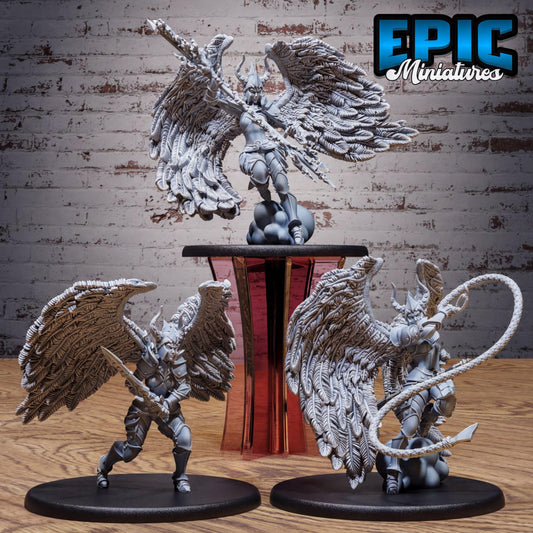 three detailed figurines of winged characters, each with distinct poses and weapons, displayed on a wooden surface against a brick wall background.