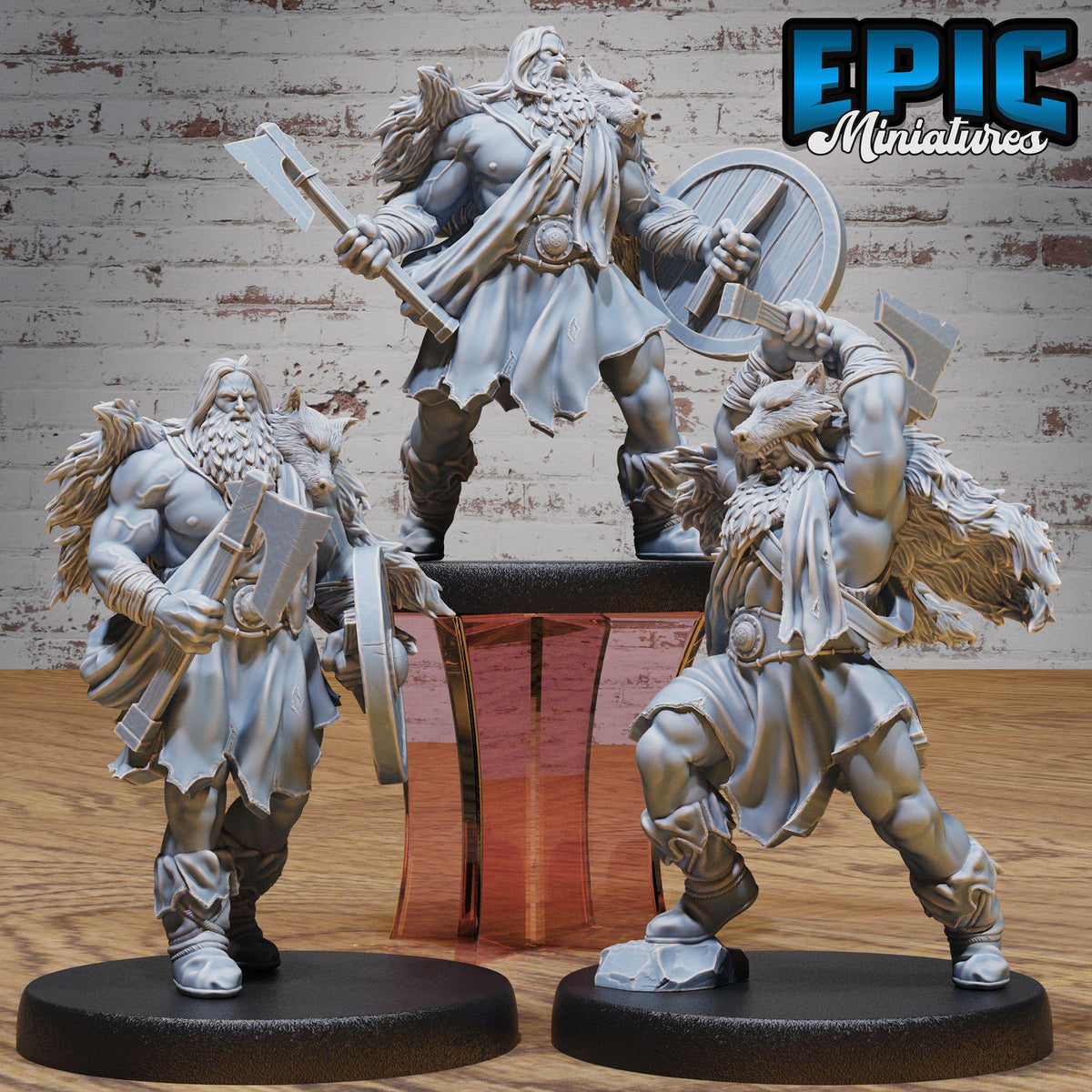 three detailed figurines of muscular, bearded men in battle attire, each holding various weapons such as swords and shields. The figurines are displayed on black bases, and the background is a brick wall.