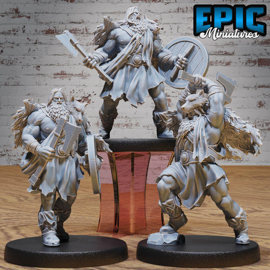 three detailed figurines of muscular, bearded men in battle attire, each holding various weapons such as swords and shields. The figurines are displayed on black bases, and the background is a brick wall.