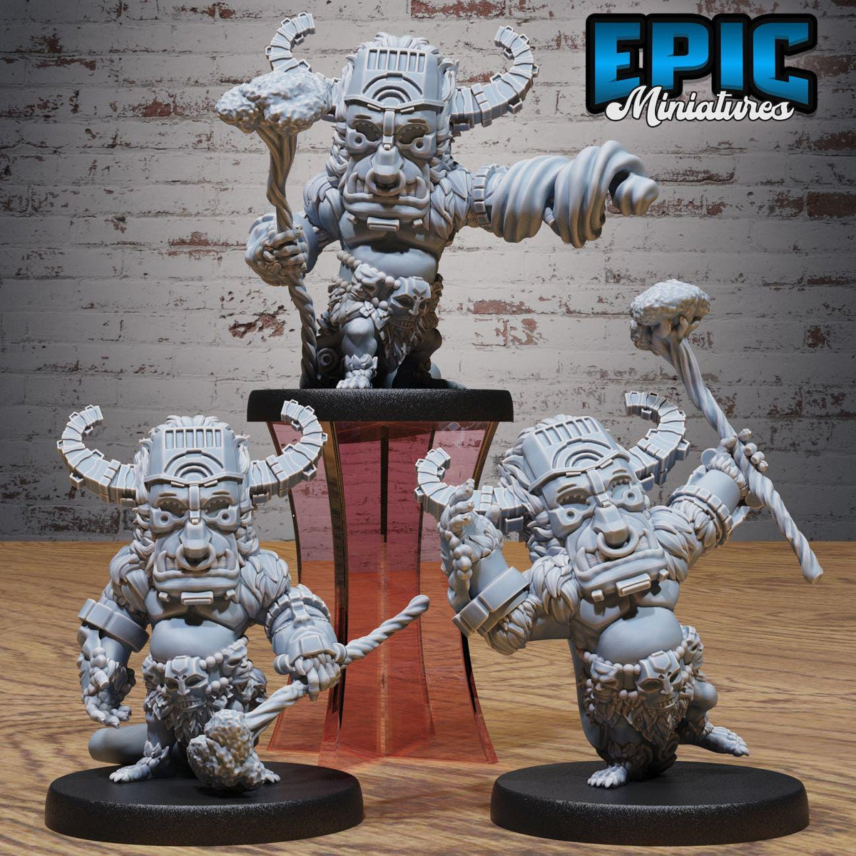 three miniature figurines of fantastical creatures, each with unique features and weapons, displayed on a stand against a brick wall background.