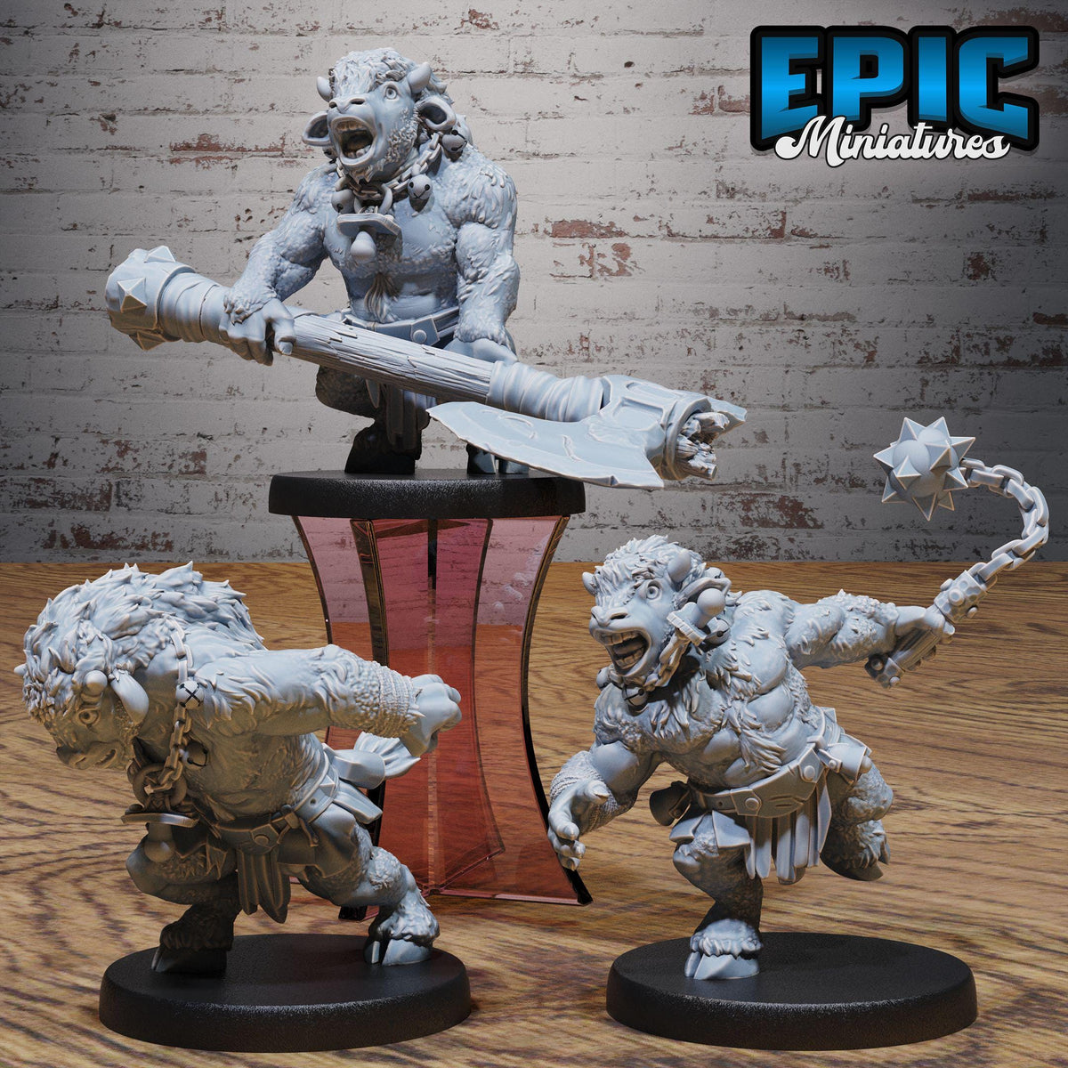 three miniature figurines of fantastical creatures, including a large, muscular monster-like creature, a smaller, furry creature, and a creature with sharp teeth and claws. The figurines are displayed on a wooden surface against a brick wall background.