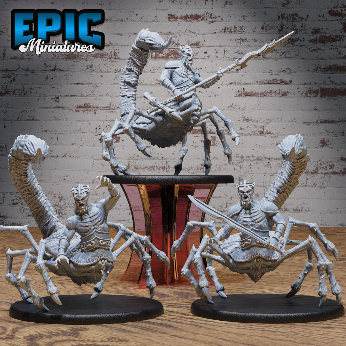 three detailed figurines of fantastical creatures, including a spider-like creature, a winged creature, and a creature with a sword. The figurines are displayed on a wooden surface, with a brick wall in the background.