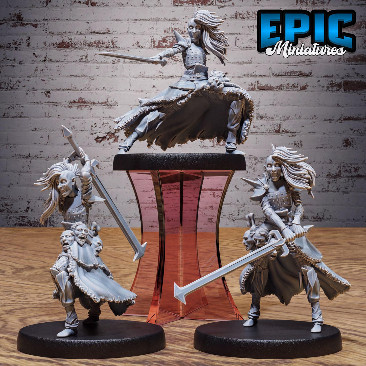three figurines of female characters, each holding a sword and standing on a platform. The figurines are arranged in a row, with one on the left, one in the middle, and one on the right. The background of the image is a brick wall, which provides a contrasting backdrop for the figurines.