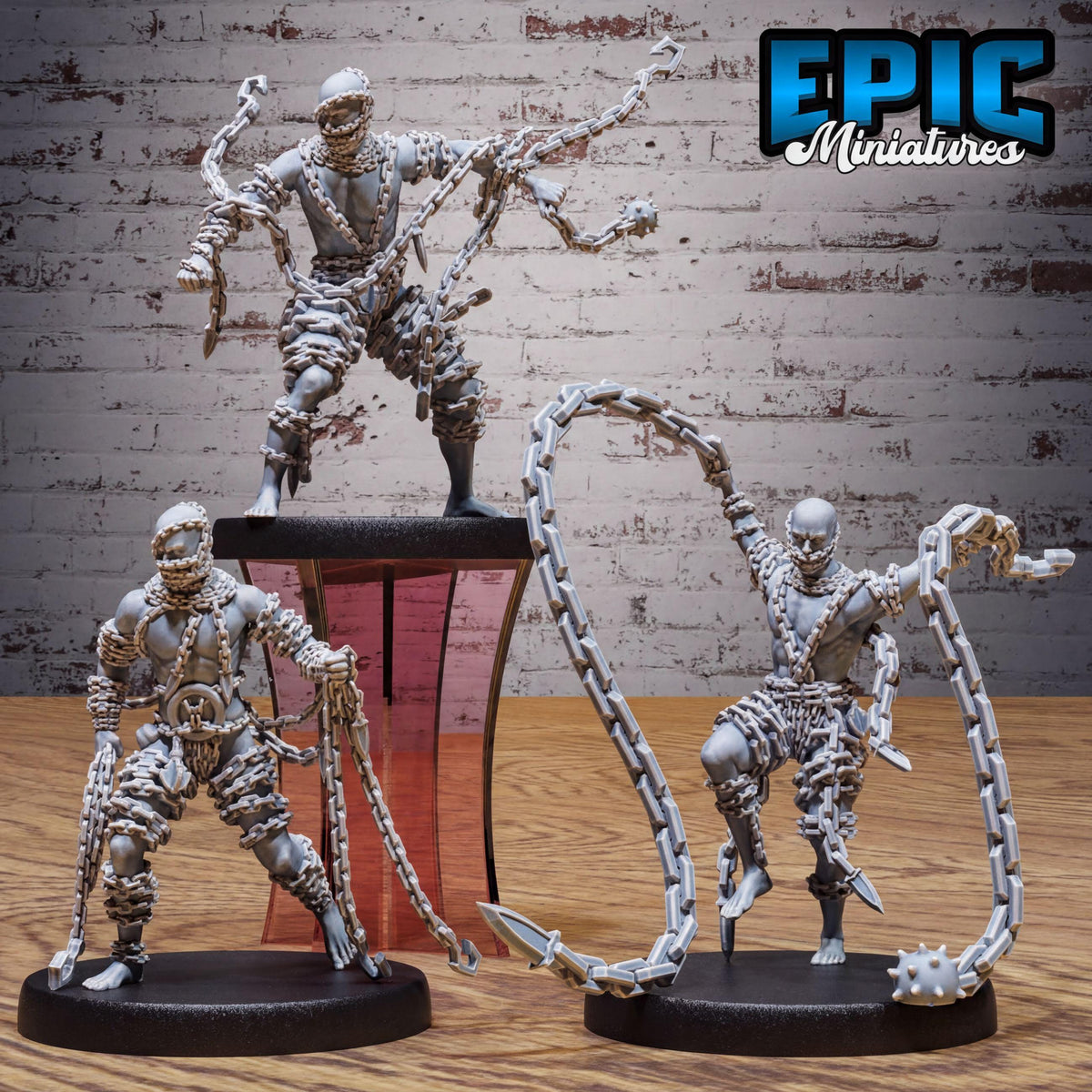 three figurines of chained, armored figures posed in various dynamic poses, set against a brick wall background.