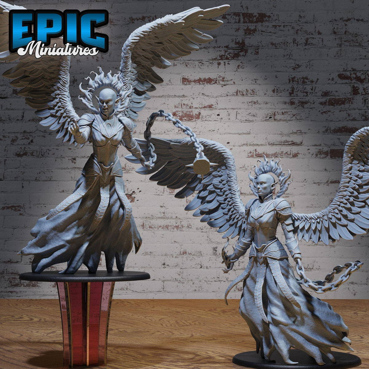 two figurines of winged, fantastical creatures, possibly resembling angels or mythical beings, standing on a table against a brick wall background.