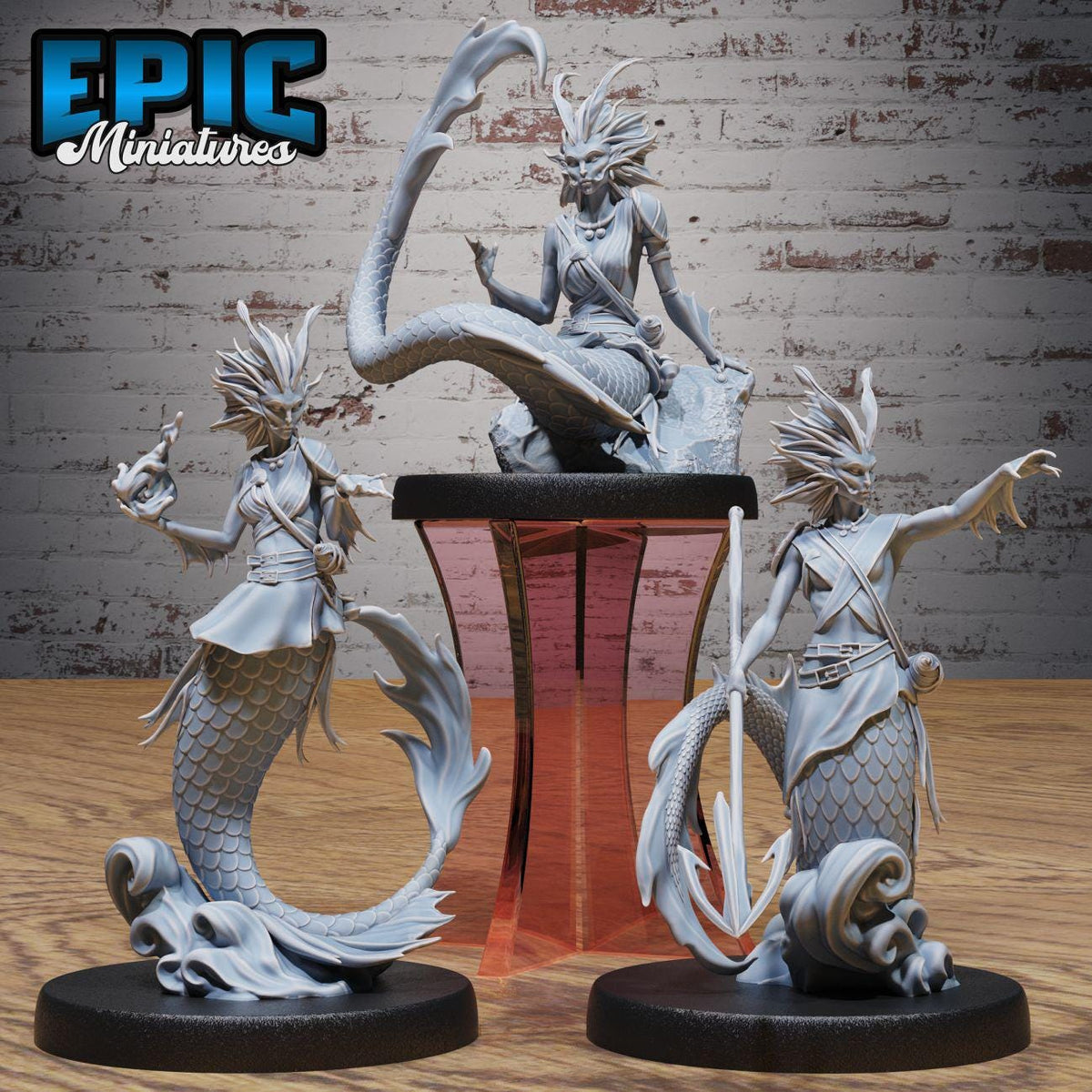 three detailed figurines of mermaids, each with unique poses and expressions, displayed on a wooden surface against a brick wall background.