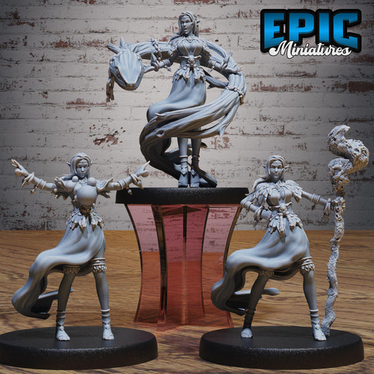 three figurines of women, each with unique poses and accessories, displayed on a stand against a brick wall background.