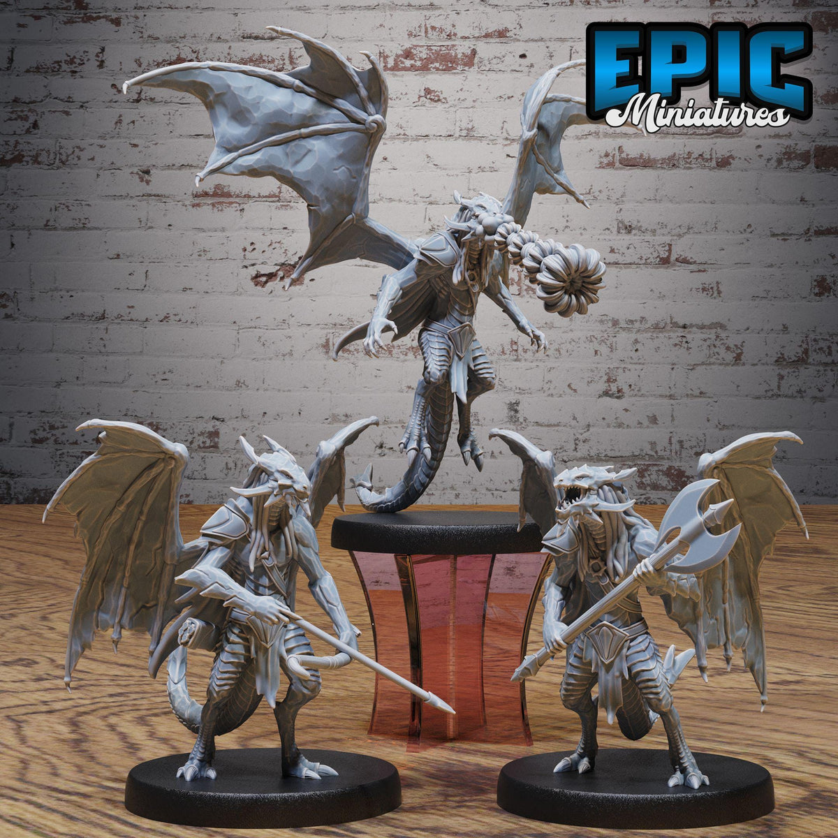 three detailed figurines of winged creatures, possibly dragon or serpent-like figures, posed on a wooden surface against a brick wall background.