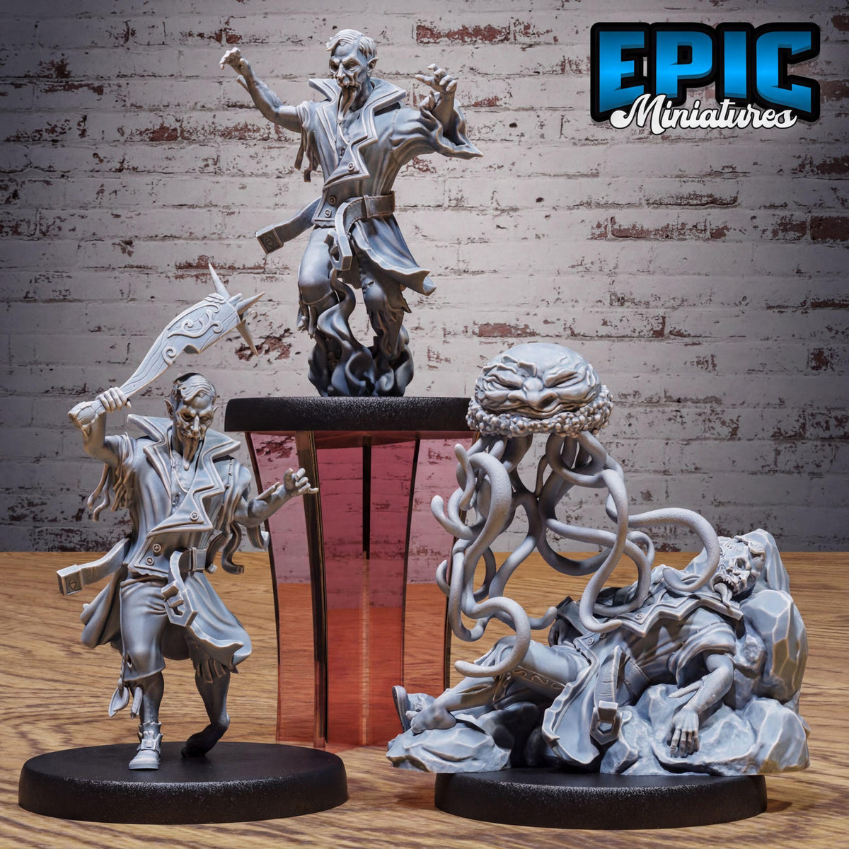 three miniature figures, including a figure with a sword, a figure with a large head, and a figure with a large body. The figures appear to be part of a collection or a set, as they are displayed together against a brick wall background.