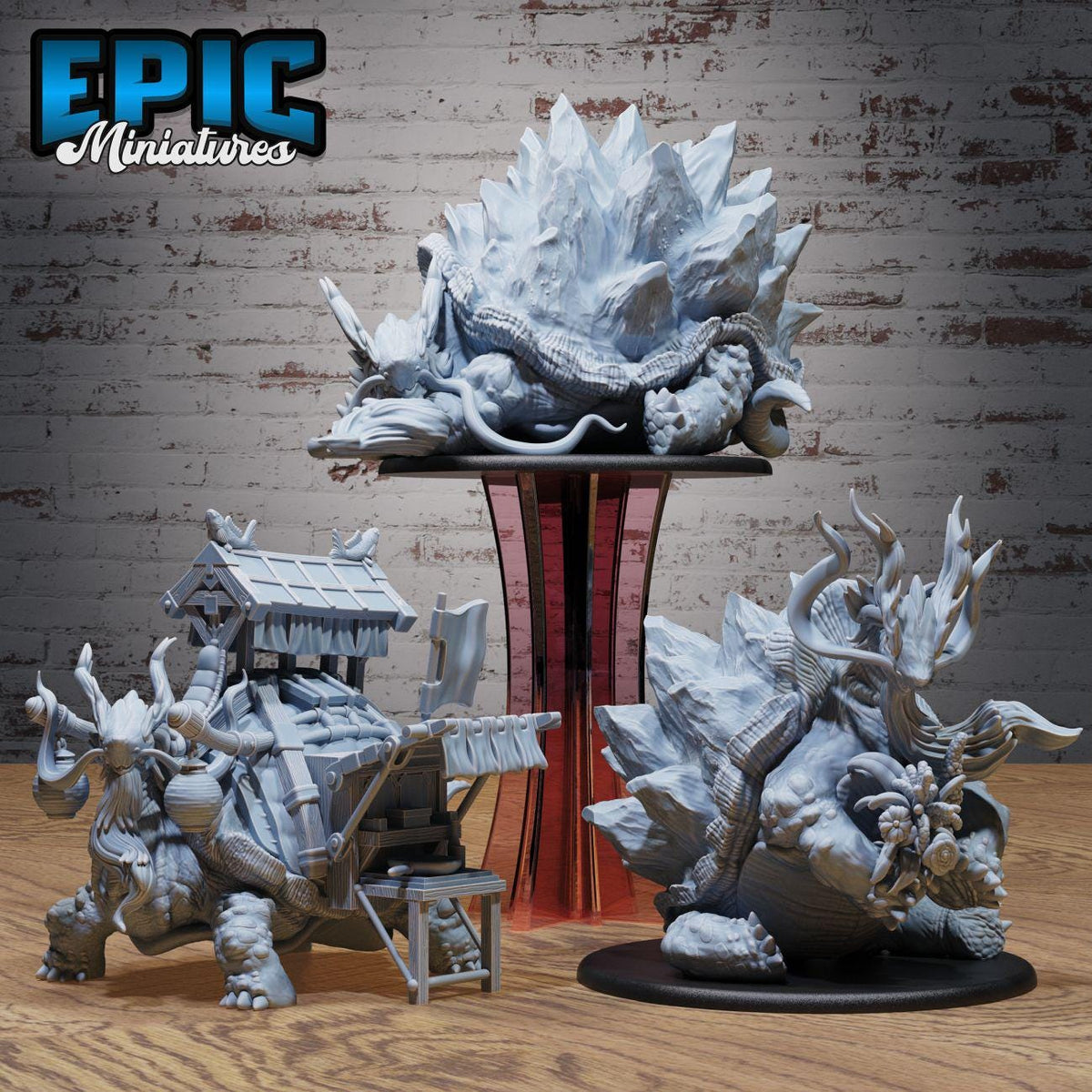 three miniature figurines of fantastical creatures, including a large dragon-like creature, a dragon-like creature with a human-like head, and a dragon-like creature with a human-like body. The figurines are displayed on a wooden surface against a brick wall background.